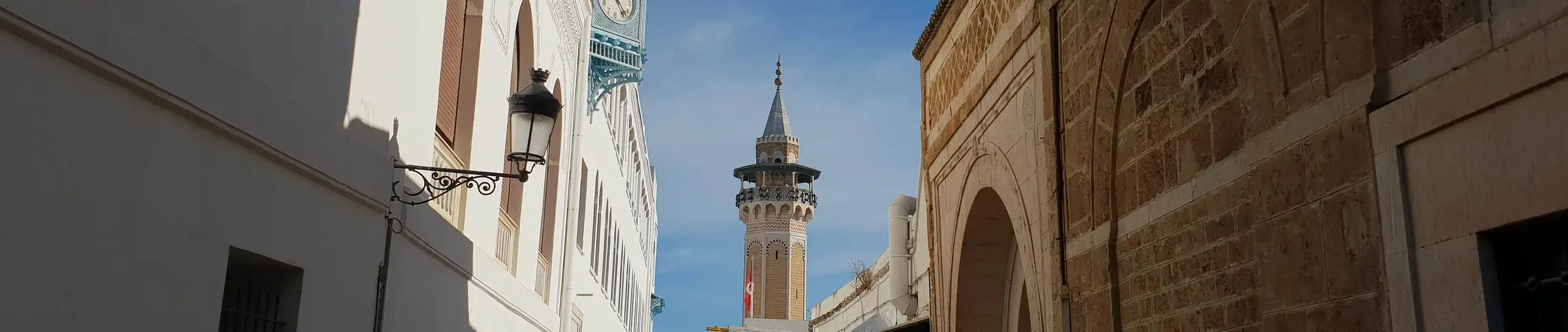 An alley in the Tunis medina between two façades, with the clock tower and a mosque minaret beyond