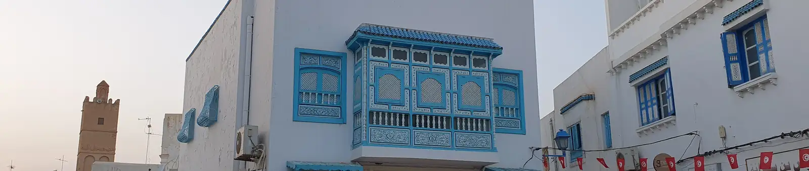 Rue de la médina de Kairouan : moucharabieh bleu et tapis suspendus devant les échoppes